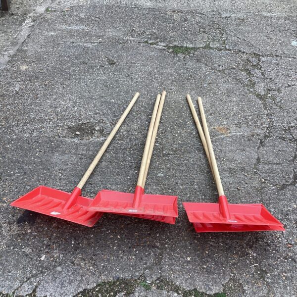 Five red plastic snow shovels with wooden handles for winter use.
