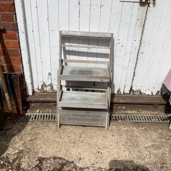 Rustic wooden garden rack with three tiers for plant display.