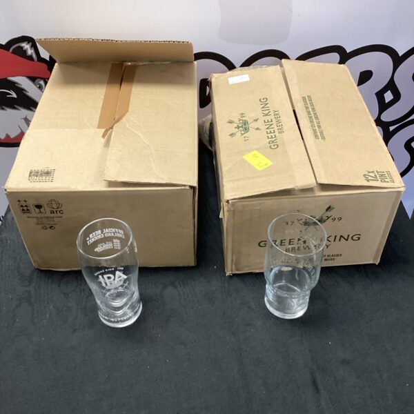 Lot of twenty-four Greene King IPA pint glasses stacked in a box.