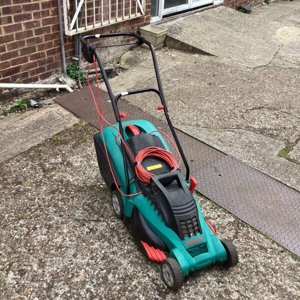 Green Bosch electric lawnmower in a garden setting.