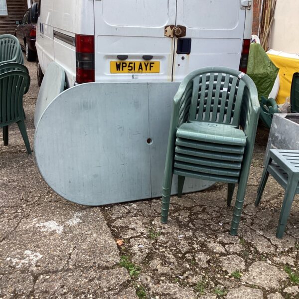 Used plastic garden table and six chairs in a garden setting.