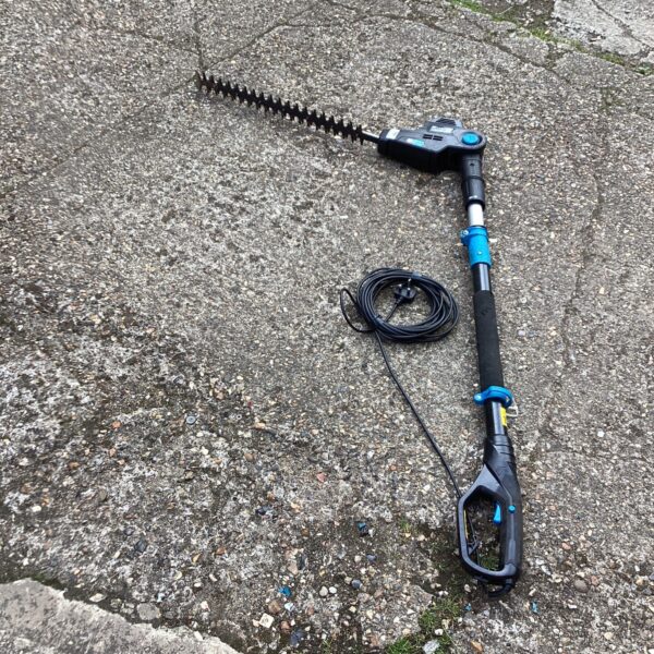 Mac hedge cutter with extended reach handle in a garden setting.