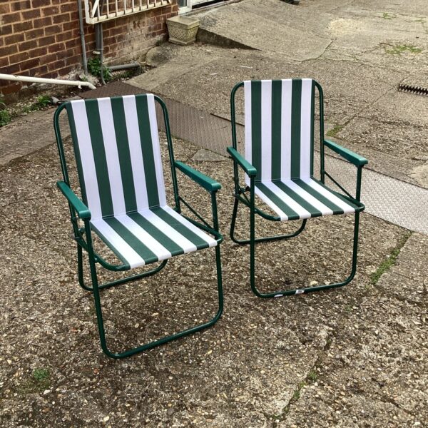 Two vintage striped folding camping chairs in a garden setting.