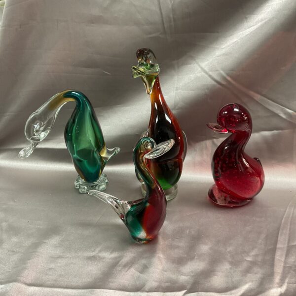 Group of four colourful glass ducks on a neutral background.