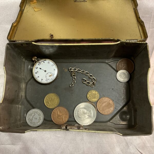 Open vintage tin box with silver watch and coins inside.