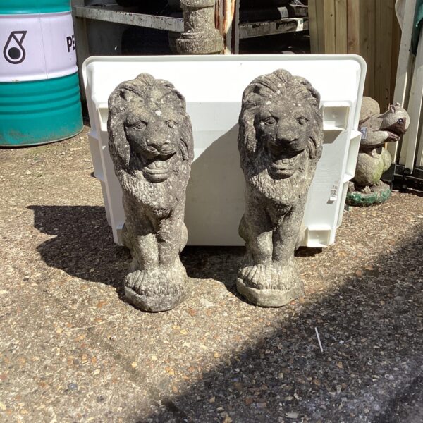 Two stone effect garden lion ornaments in a garden setting.