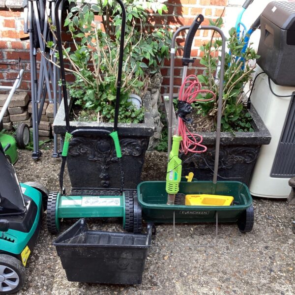 Vintage garden spreader and lawn mower in a garden setting.