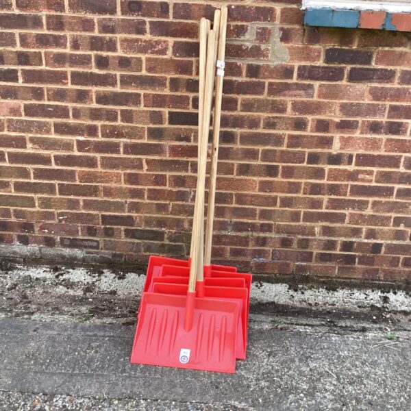 Five red plastic snow shovels with wooden handles for winter use.