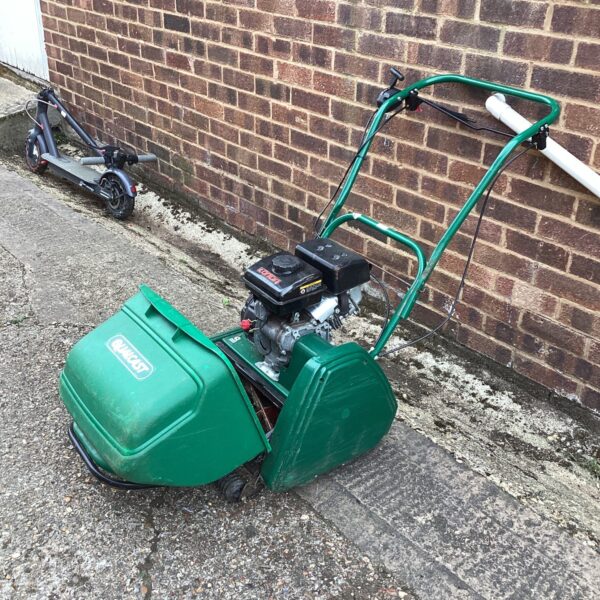 Vintage Qualcast lawn mower in a garden setting, showing signs of wear.