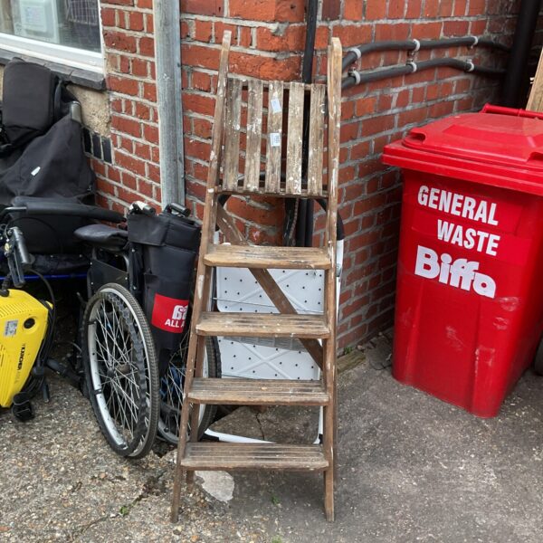 Vintage wooden step ladder leaning against a brick wall.