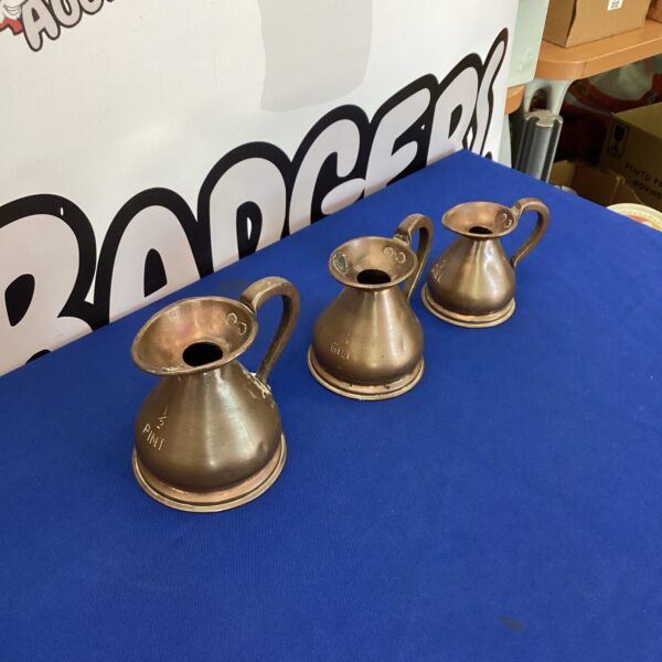 Three vintage copper haystack measuring jugs on a neutral background.