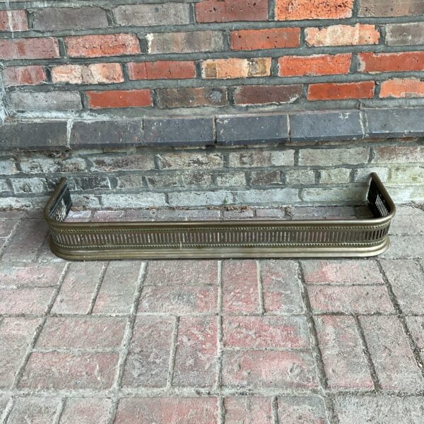 Ornate vintage brass fireplace fender for hearth protection.