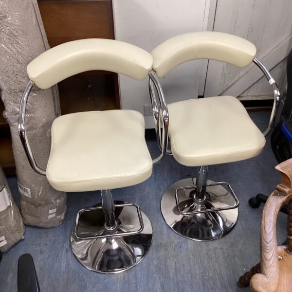 Cream leather bar stools with chrome bases and adjustable height.