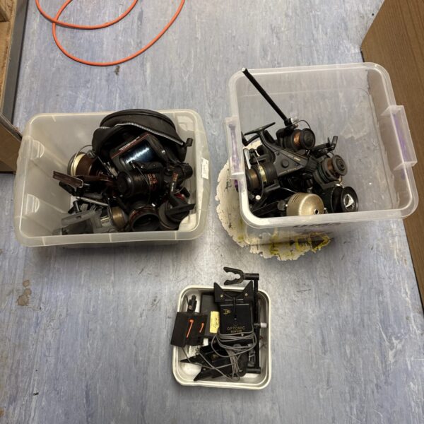 Assorted vintage fishing reels and bite alarm sensors in tubs.