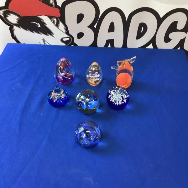 Collection of colourful Murano glass paperweights on a blue surface.