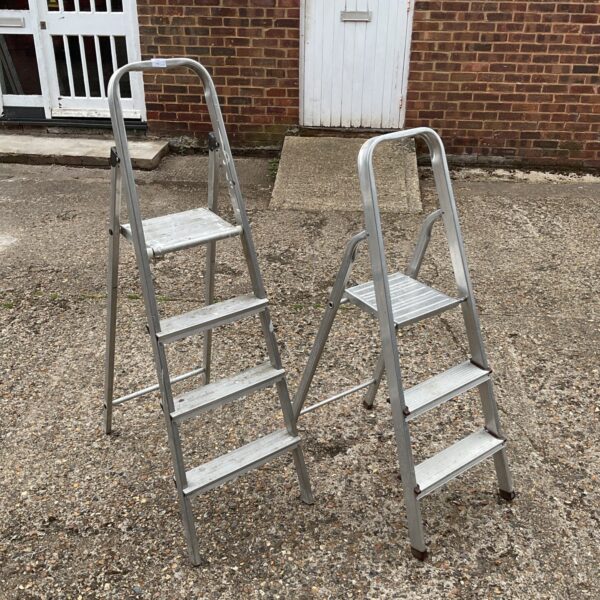 Two aluminium step ladders leaning against a wall.