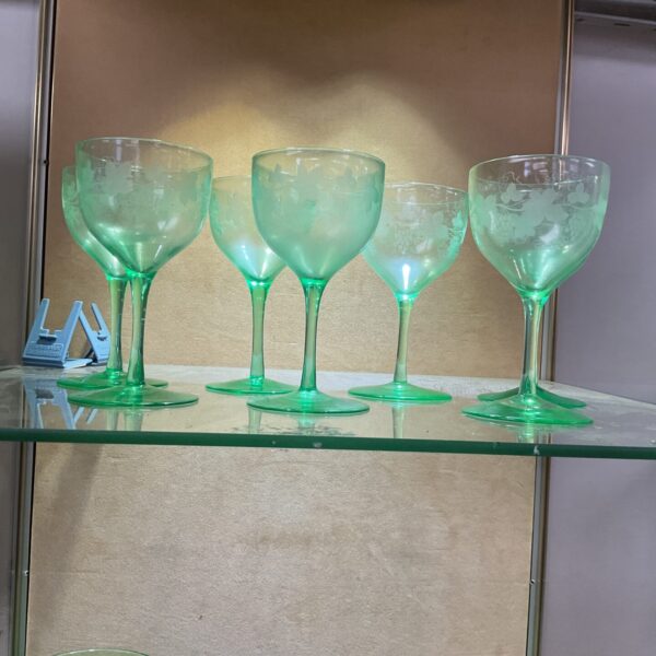 Seven green uranium wine glasses with hand-engraved floral designs.