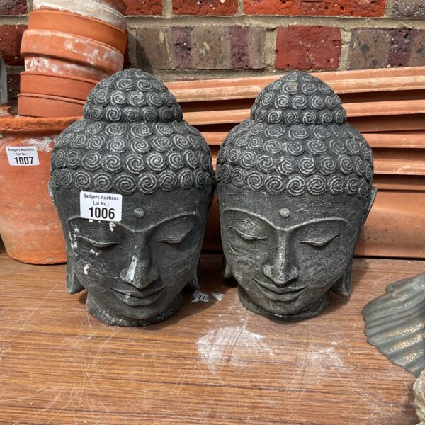 Two weathered stone Buddha heads in a garden setting.