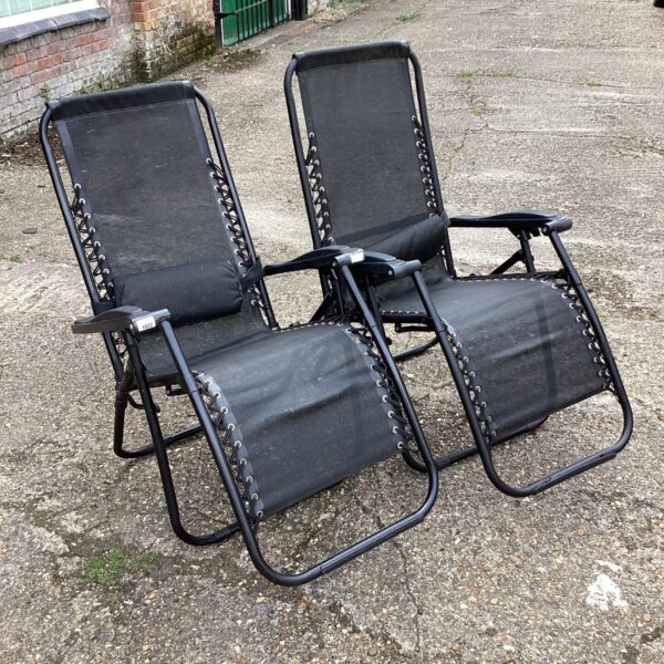 Two black folding garden loungers in a garden setting.