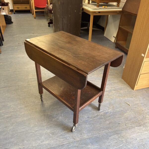 Vintage mahogany drop leaf table with wheels and a lower shelf.