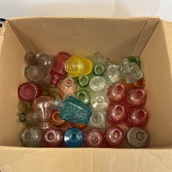 Assorted colourful vintage glass bottles and vases in a cardboard box.
