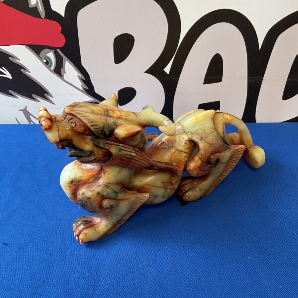 Detailed vintage Chinese soapstone dragon sculpture on blue background.