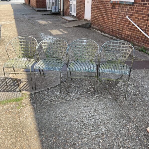 Lot of four vintage wrought iron garden chairs in a garden setting.