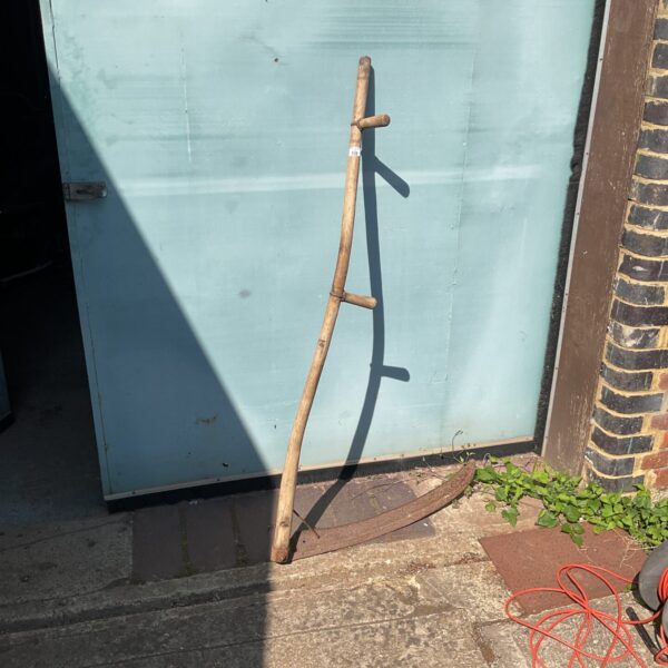 Vintage scythe with wooden handle leaning against a door.