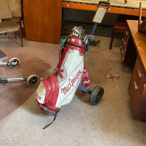Vintage MacGregor golf bag with clubs and trolley in a room setting.