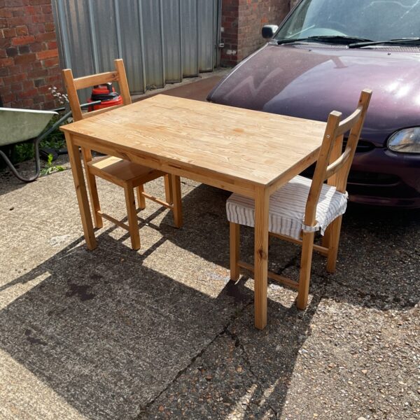 Rustic pine kitchen table and two chairs in a domestic setting.