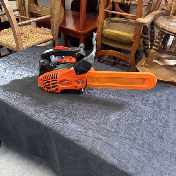 Orange Timberpro chainsaw resting on antique furniture.