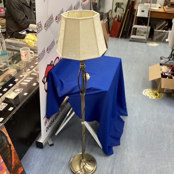 Vintage brushed brass standard lamp with cream shade on blue backdrop.