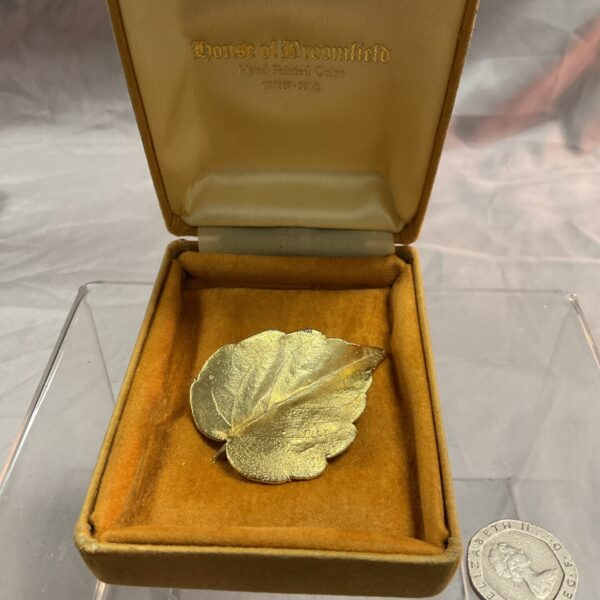 Vintage gold leaf brooch on a patterned background.