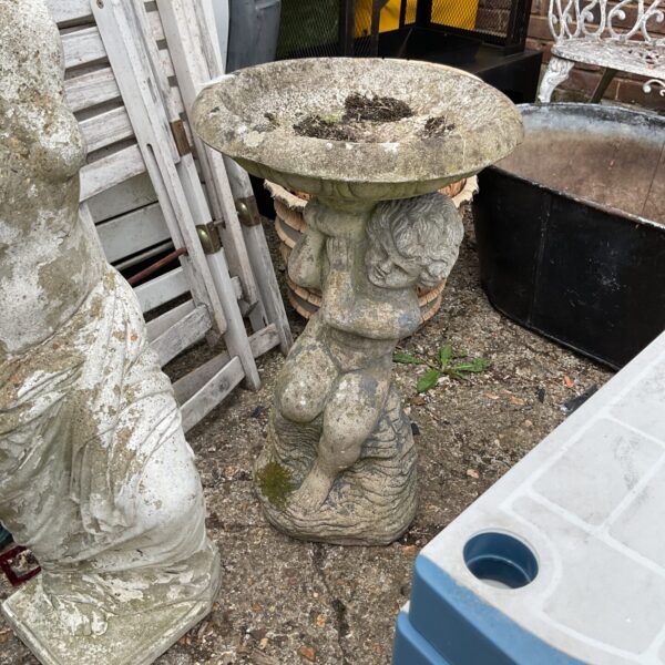 Vintage stone birdbath ornament with cherub in garden setting.