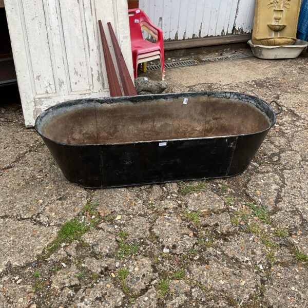Large vintage galvanised bath in a garden setting.