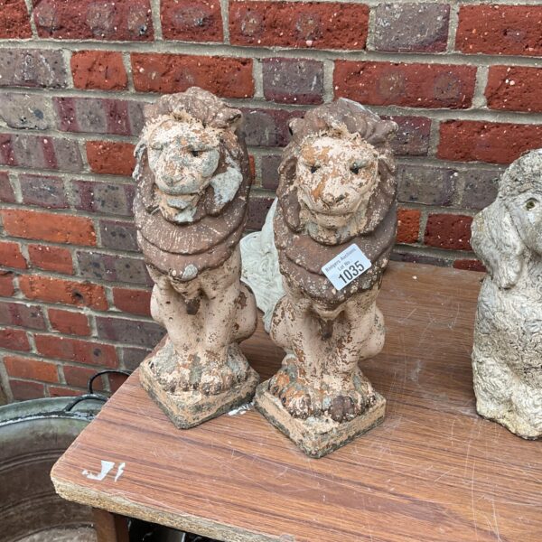 Pair of weathered stone garden lion ornaments in a garden setting.