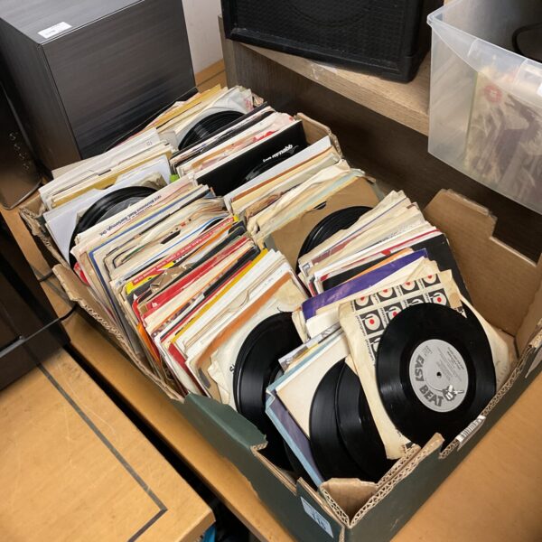 Stack of vintage 7 inch vinyl records in a cardboard box.