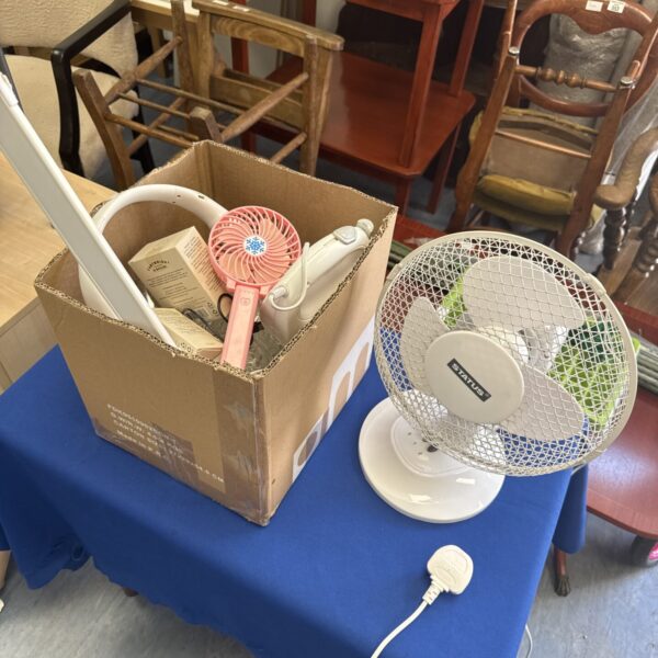 Assorted personal fans and a Status desk fan on a table.