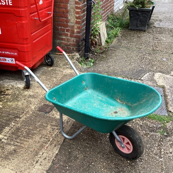 Green plastic wheelbarrow for garden use and landscaping tasks.