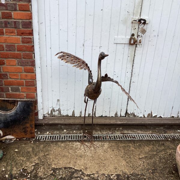 Rustic metal garden heron sculpture in an outdoor setting.