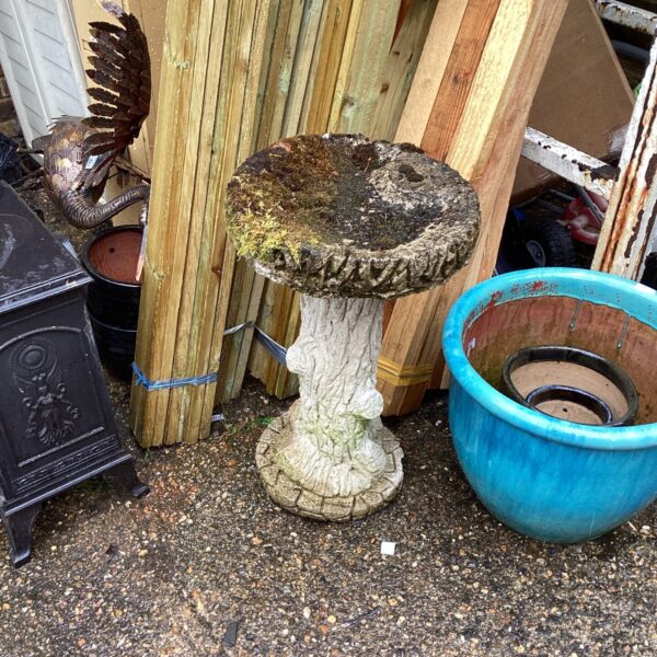 Weathered stone garden bird bath with tiered design in a garden setting.