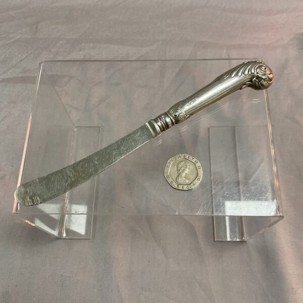 Antique silver butter knife with ornate handle and hallmarks.
