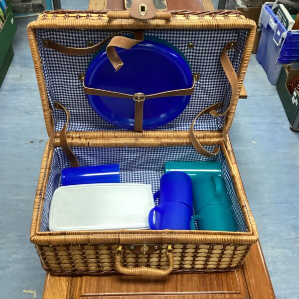 Open vintage wicker picnic basket with blue lining and contents.