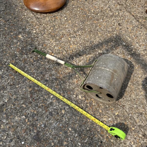 Vintage metal garden roller with wooden handle for lawn compaction.