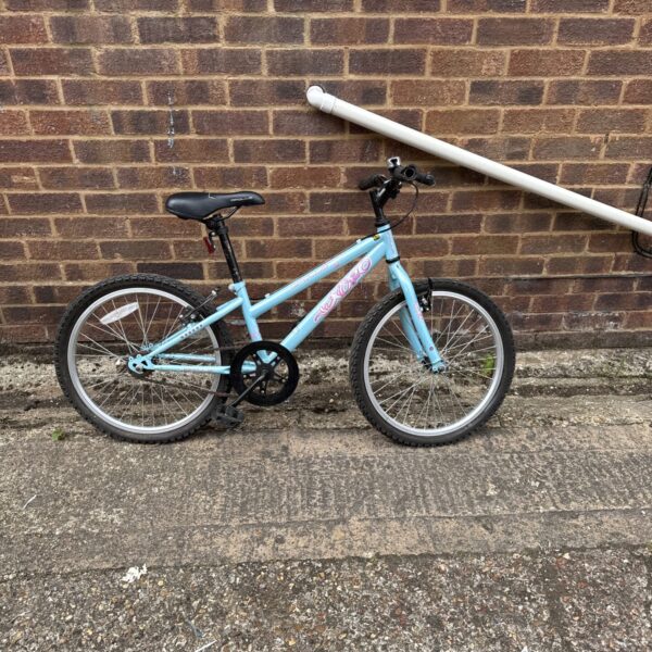 Light blue Apollo girls bike leaning against brick wall.
