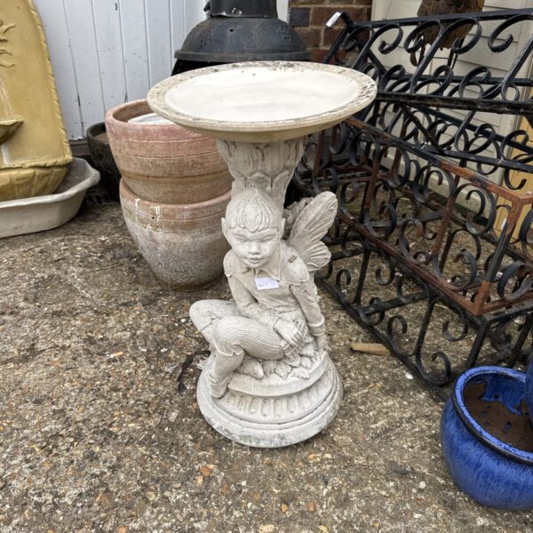 Detailed concrete Peter Pan bird bath in a garden setting.