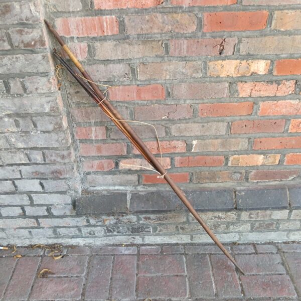 Antique tribal bow and arrows leaning against a brick wall.
