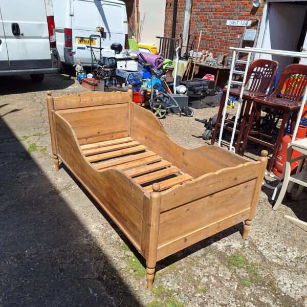 Side view of a vintage pine bed frame in a garden setting.