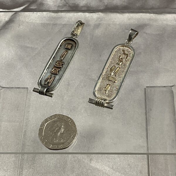 Two silver Egyptian ingot pendants on a neutral background.