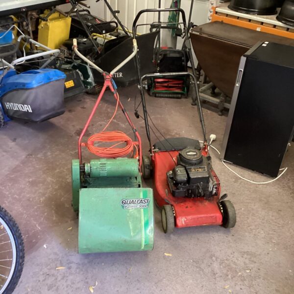Side view of a vintage Qualcast electric lawnmower in a garden setting.